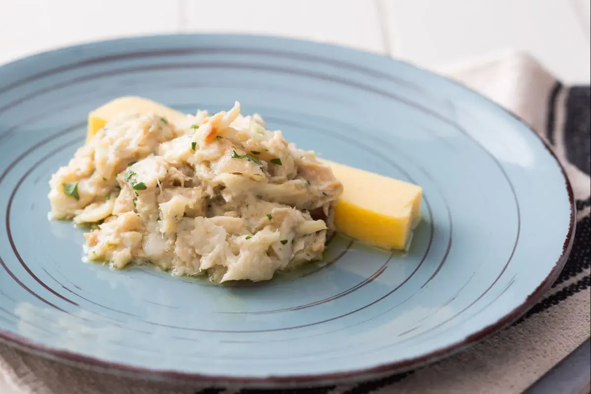 Baccalà alla Vicentina, ein cremiges Stockfischgericht mit Petersilie, serviert mit einem Stück Polenta auf einem blauen Teller.