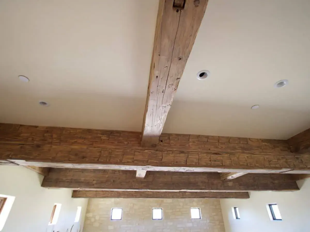 Poutres apparentes en bois ciré, patinées par le temps, soutenant un plafond blanc avec des spots encastrés.