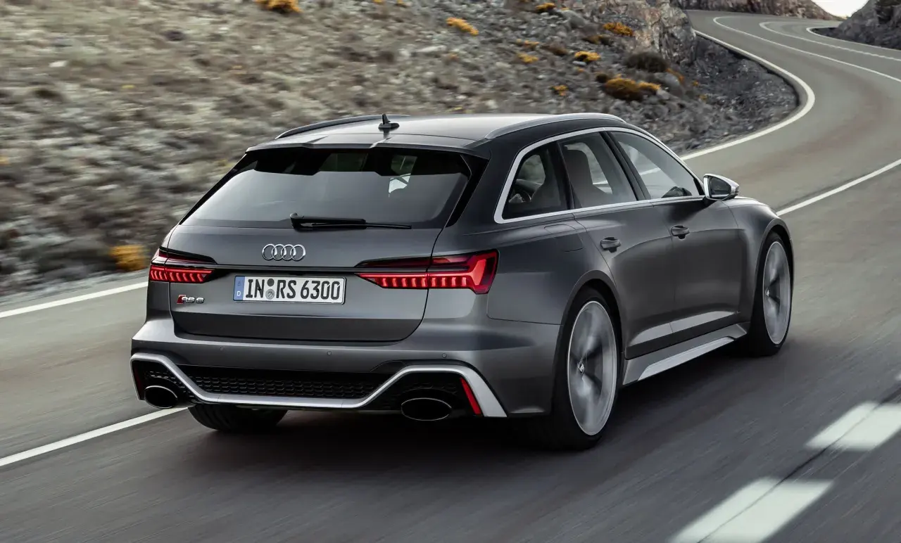 El Audi RS6 ranchera gris oscuro acelera por una carretera sinuosa entre montañas.