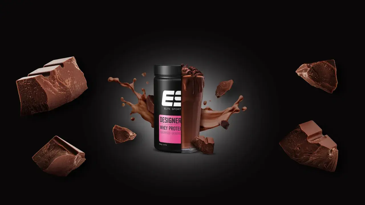 Schokoladenstückchen umgeben einen Becher Designer Whey Protein. Die Frage, ob Proteinpulver krebserregend ist, bleibt unbeantwortet.