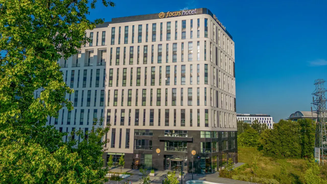 Nowoczesny budynek Focus Hotel Premium Warszawa z zielenią i błękitnym niebem. Idealne miejsce na pobyt.
