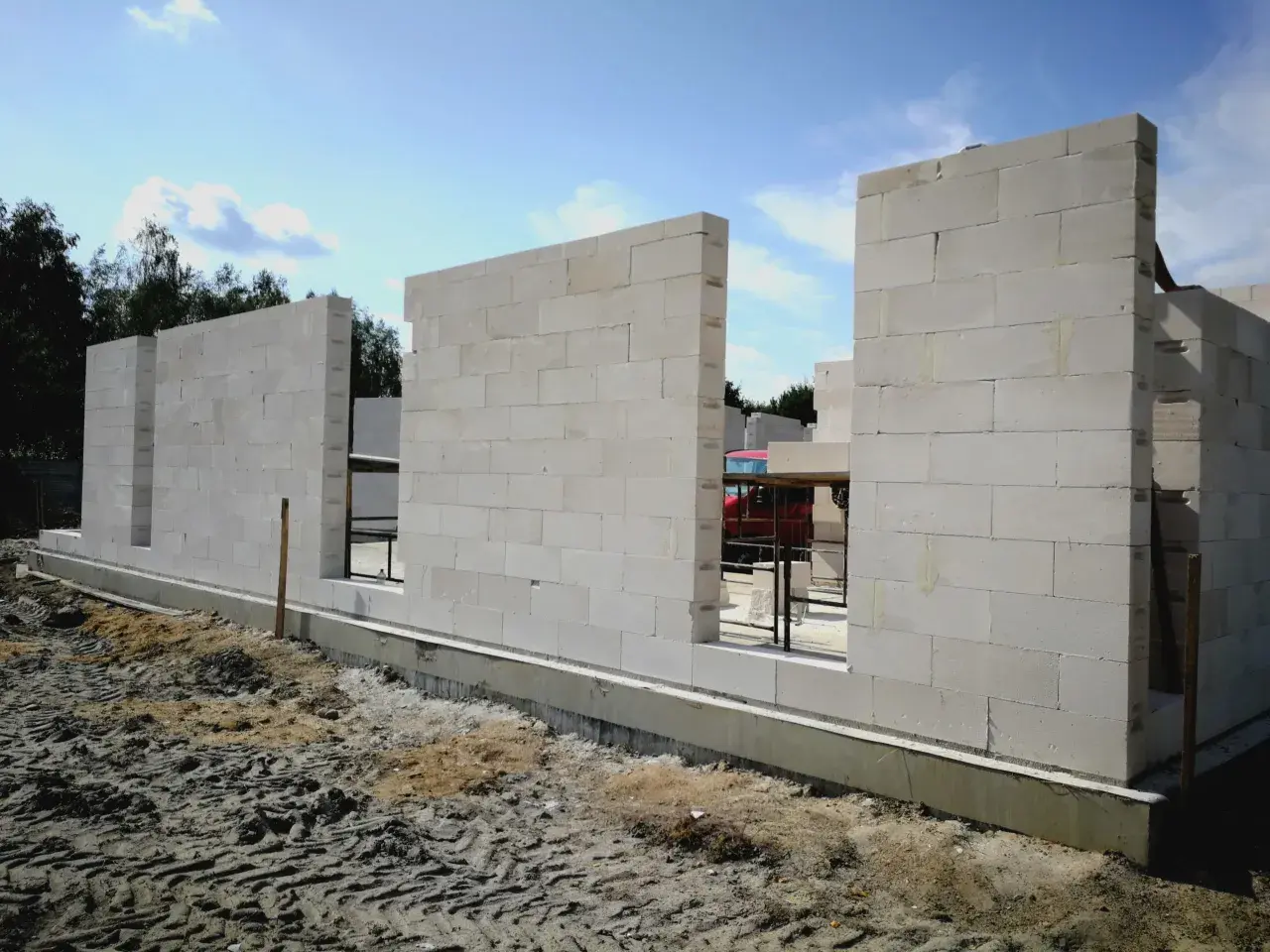 Budowa domu z bloczków z betonu komórkowego. Ściany wznoszą się nad fundamentem, tworząc zarys pomieszczeń.