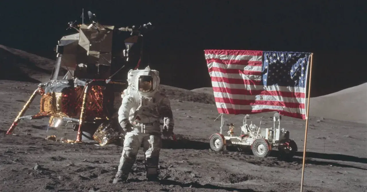 Astronaut w skafandrze podczas spaceru po księżycu, obok lądownika i łazika z amerykańską flagą.