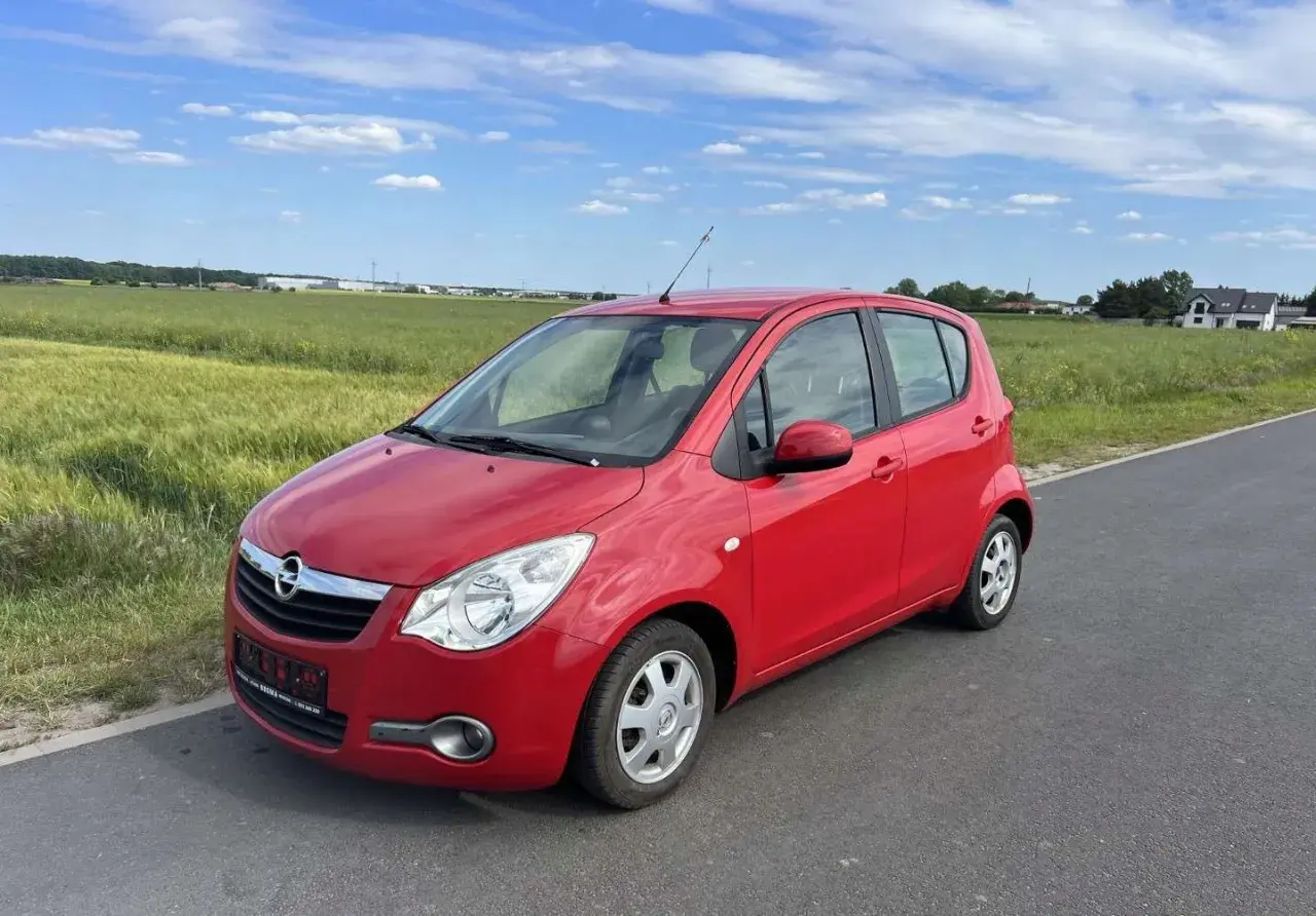 Czerwony Opel Agila 1.2 na tle zielonych pól i błękitnego nieba.