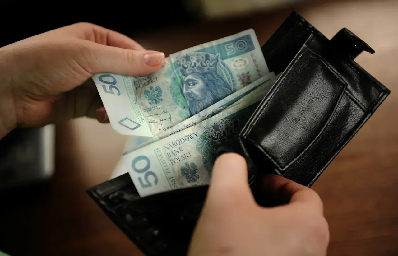 Ręce wkładają polskie banknoty 50 zł do czarnego portfela. To kieszonkowe dla dziecka na drobne wydatki.