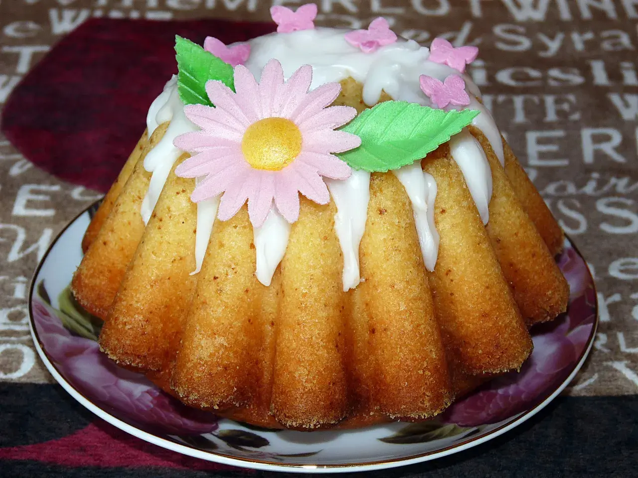 Babka jogurtowa cytrynowa ozdobiona lukrem, różowym kwiatkiem i motylkami. Idealna na wiosenne popołudnie.