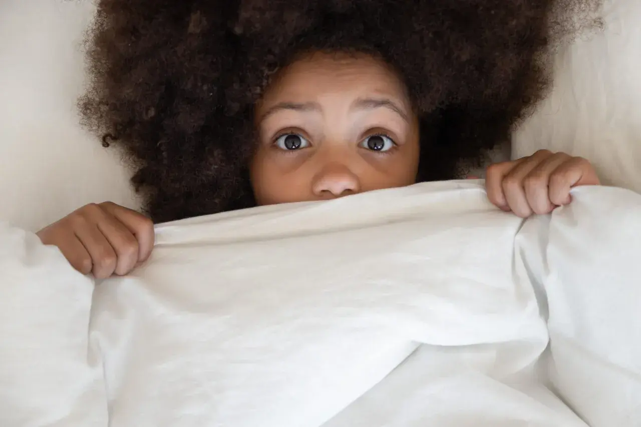 Occhi sgranati di bambino nel letto, nascosto sotto le coperte, con un'espressione di pavor notturno.