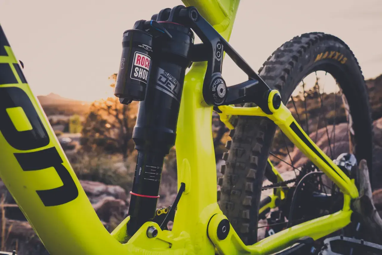 Close-up of a bright yellow mountain bike's rear suspension. The Rock Shox Super Deluxe shock has a length chart visible.