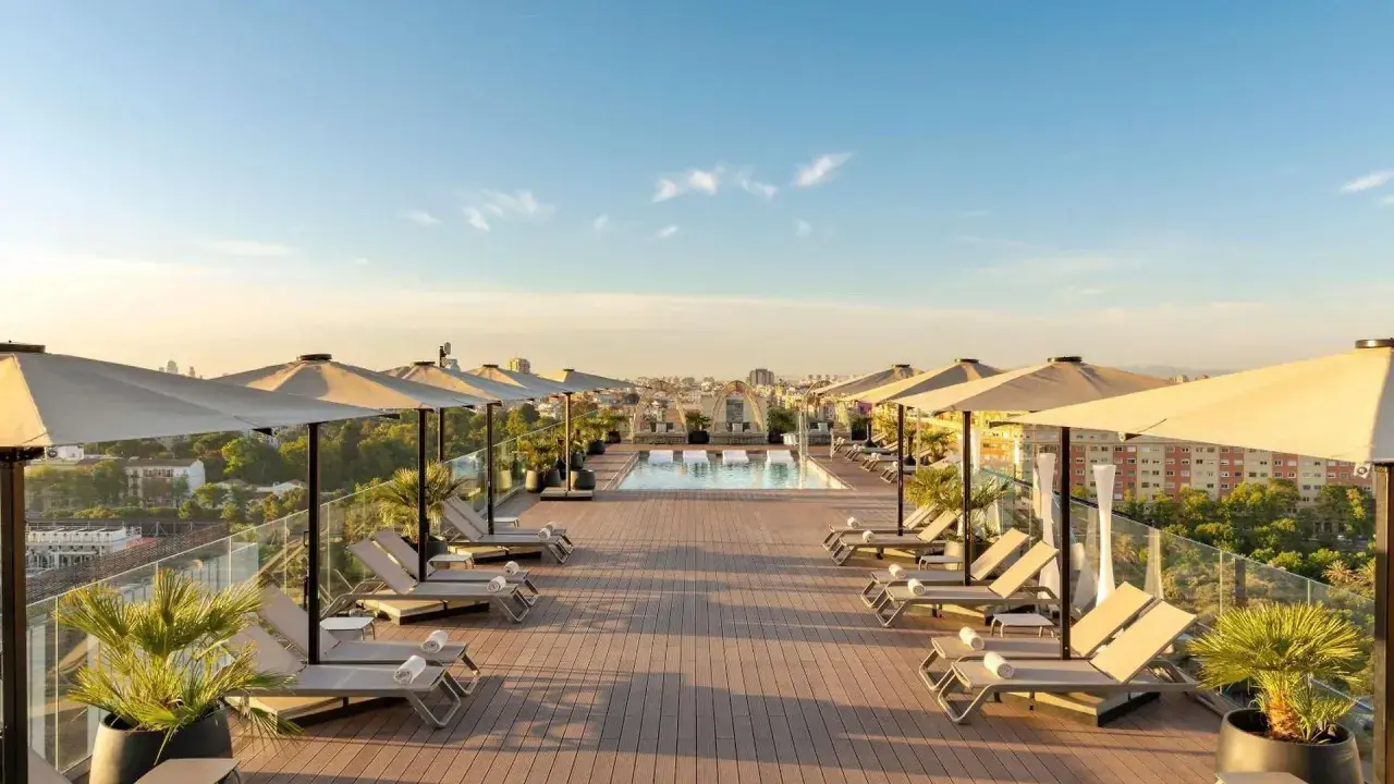 Terraza con piscina y tumbonas en el Novotel Valencia, vistas a la ciudad al atardecer.