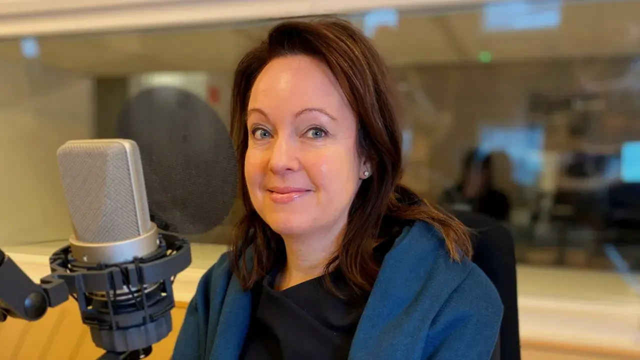 Anna Borg ler mot kameran i en inspelningsstudio, med en mikrofon framför sig.