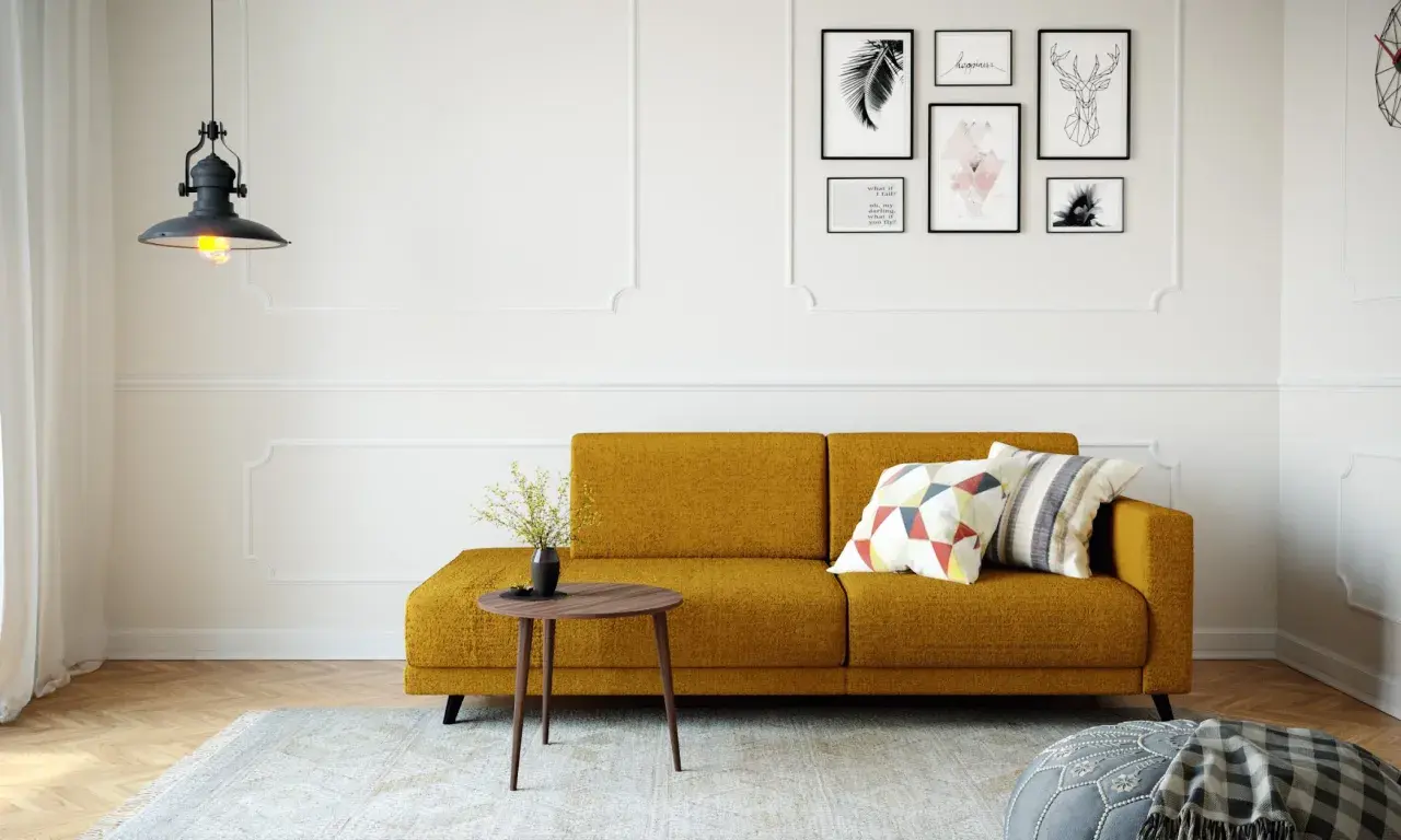 Ein gemütliches kleines Wohnzimmer einrichten mit einem senfgelben Sofa, Kissen, einem Beistelltisch und Wandkunst.