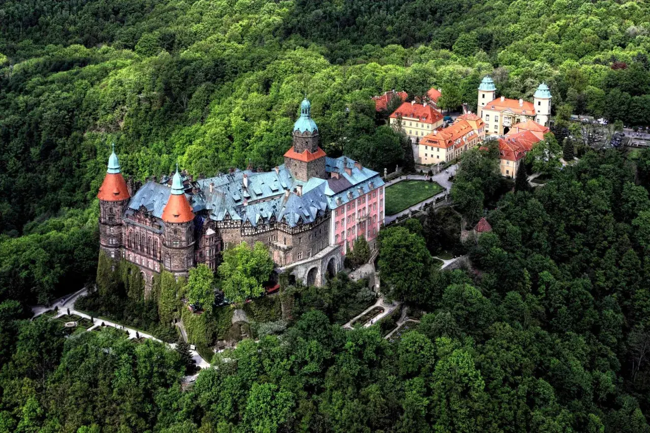Zamek **Chudów** otoczony bujną zielenią, z charakterystycznymi wieżami i czerwonymi dachami, wygląda jak z bajki.