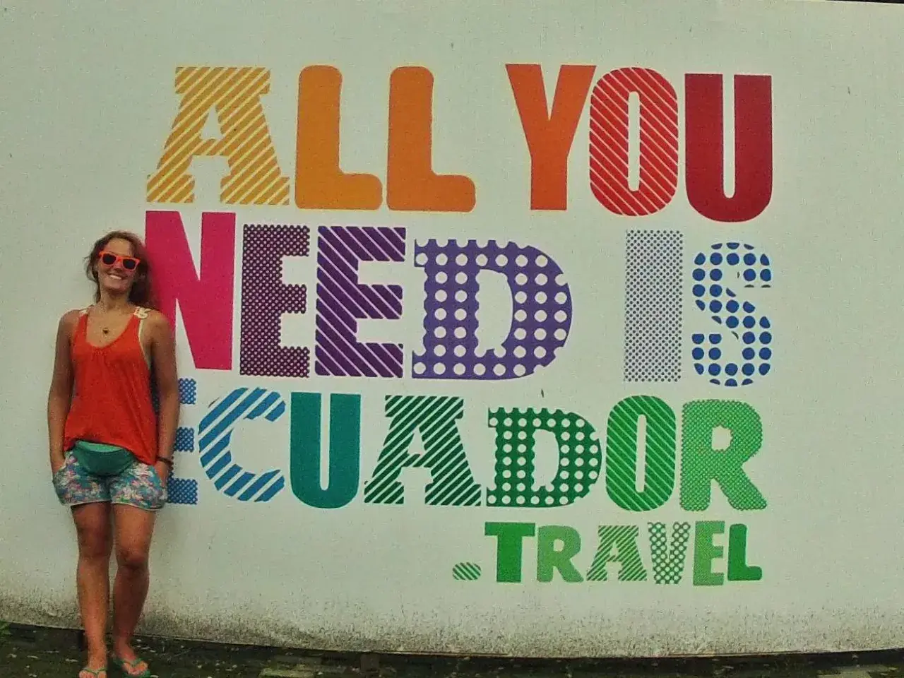 Uśmiechnięta turystka w Vilcabamba pozuje na tle kolorowego napisu "All you need is Ecuador. Travel".