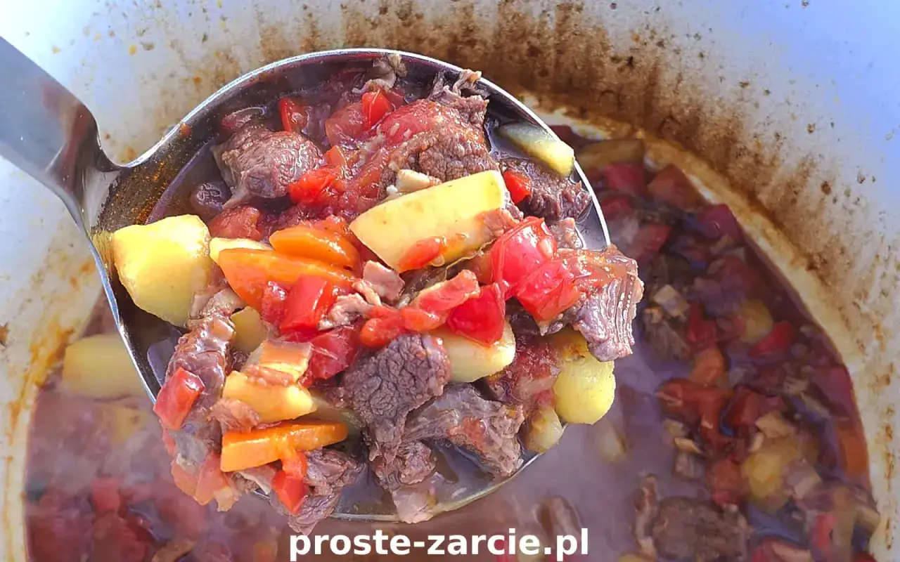 Gulasz z kociołka żeliwnego na ognisku, pełen mięsa, ziemniaków i warzyw, paruje apetycznie.