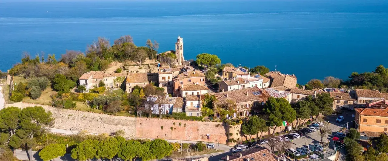 Borgo medievale di Gabicce Mare cosa vedere: un incantevole panorama di case con tetti rossi, un campanile e il blu del mare Adriatico.