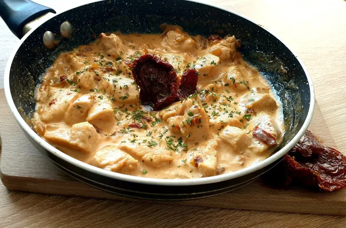 Kawałki kurczaka w kremowym sosie z suszonymi pomidorami i natką pietruszki. Danie "marry me chicken" wygląda apetycznie.