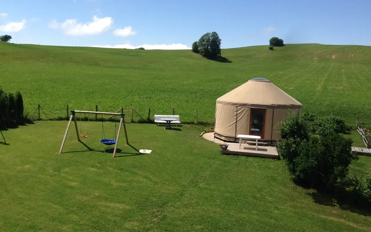 Une yourte confortable vous attend pour un séjour paisible en pleine nature, location yourte Jura. Balançoire et bancs invitent à la détente.