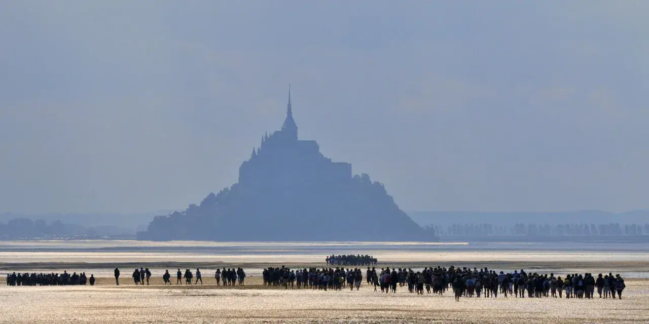 Silhouetten von Menschen auf dem Wattboden, die sich dem majestätischen Mont Saint-Michel nähern.
