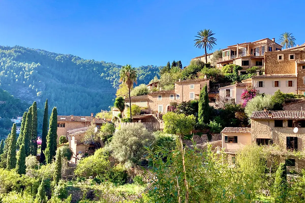 Malerische Steinhäuser schmiegen sich an einen grünen Hang. Palmen und Zypressen wachsen zwischen den Gebäuden. Ein friedlicher Anblick von Mallorca im Dezember.