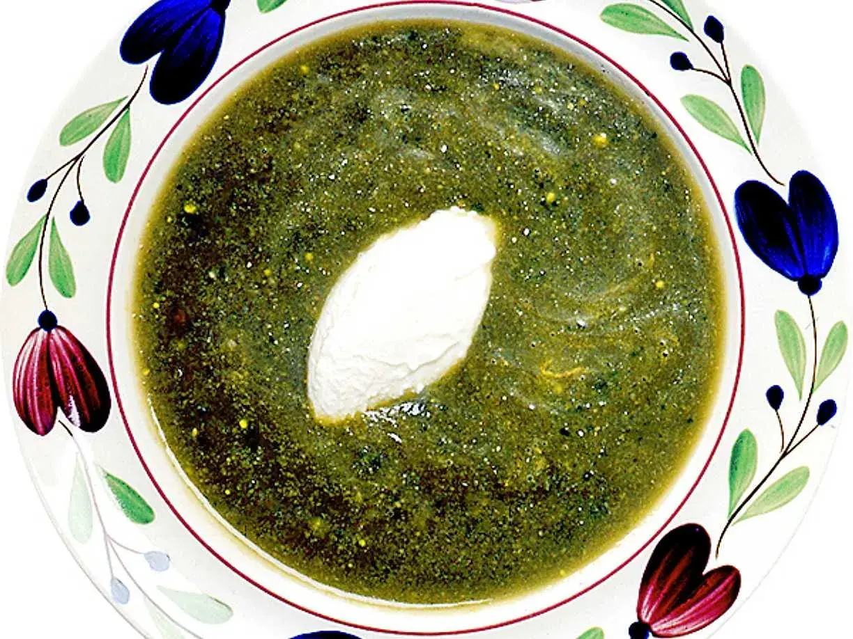 A bowl of green soup with a dollop of cream, garnished with colorful floral patterns.