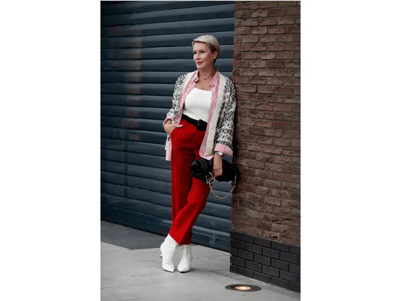 Elegancka kobieta w czerwonych spodniach i wzorzystej marynarce, z czarną torebką na łańcuszku. Stylowe czerwone spodnie stylizacje.