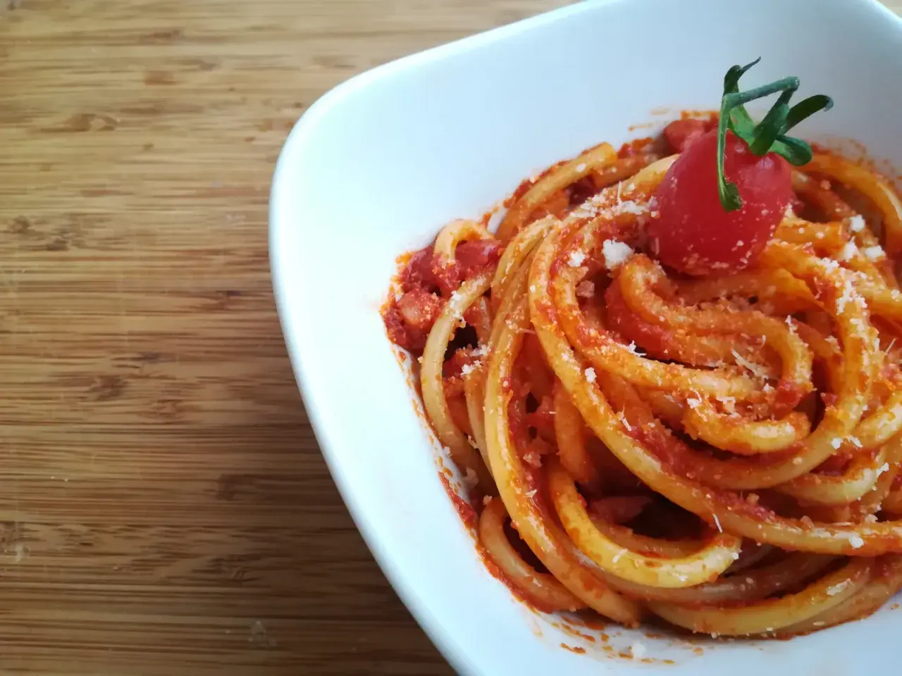 Pyszne spaghetti z sosem pomidorowym i startym parmezanem, ozdobione pomidorkiem. Idealne do przygotowania według przepisu na guanciale.