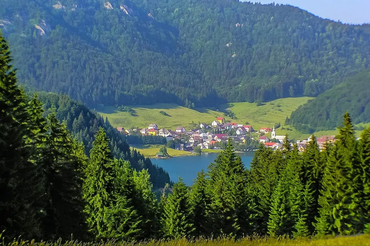 Idyllisches Dorf am See, umgeben von grünen Hügeln und Nadelwäldern. Perfekt für Slowakei Reisetipps!