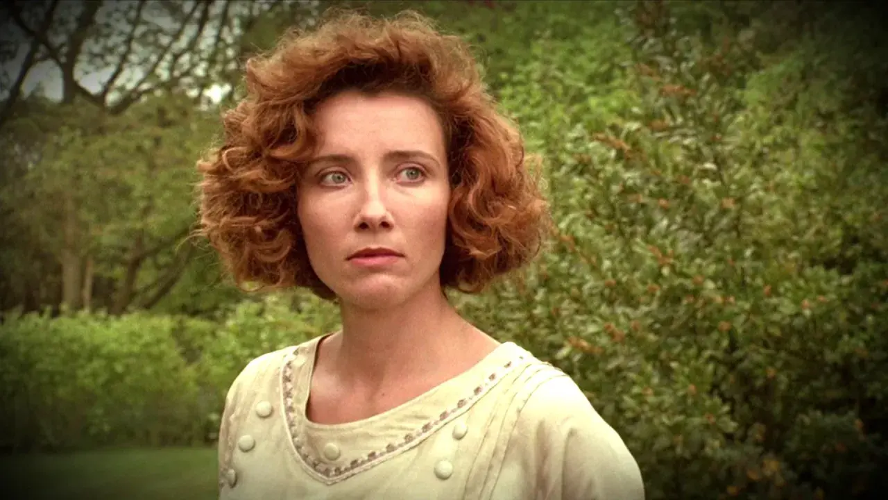 Emma Thompson w filmie, z burzą rudych loków i w jasnej sukni, spogląda zamyślona na tle zieleni.