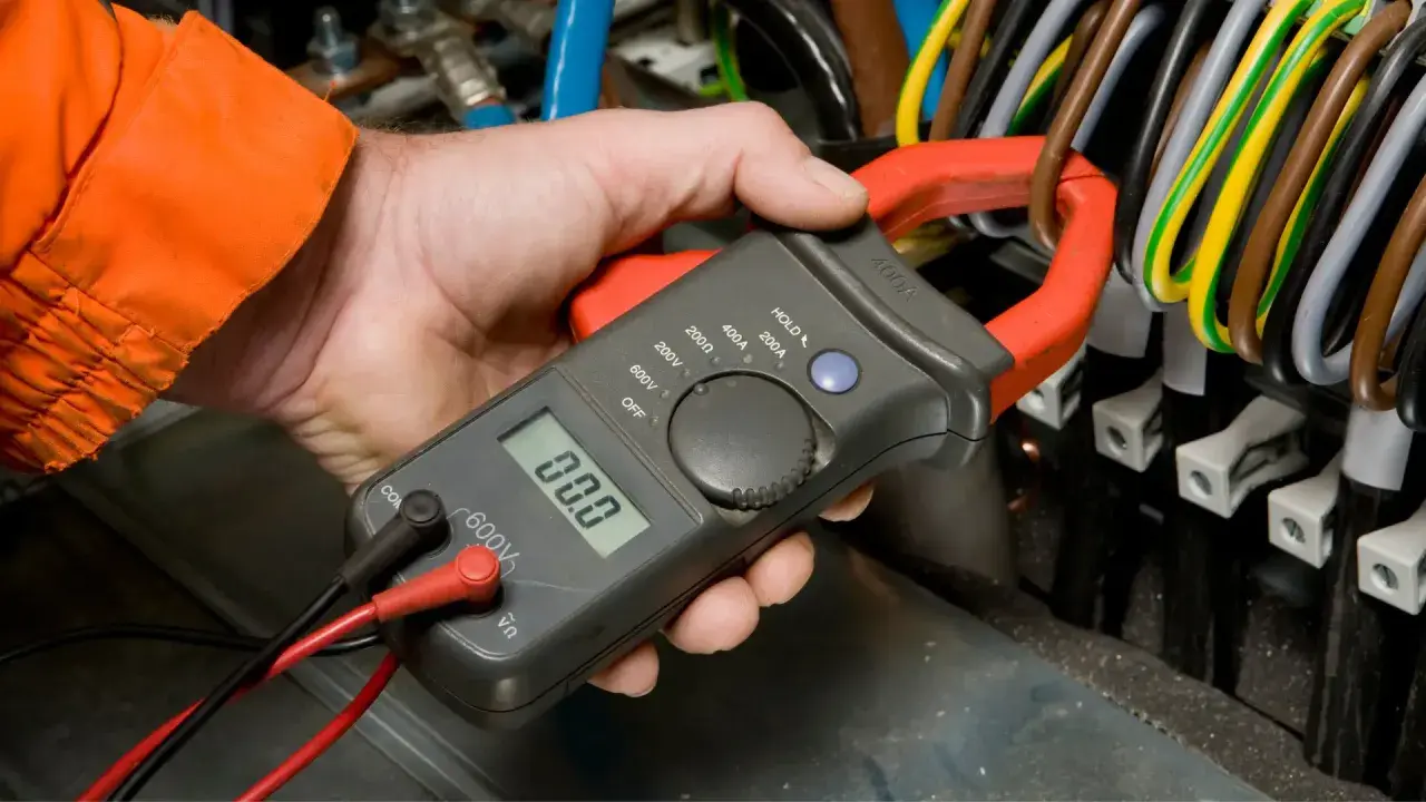 Elektryk mierzy spadek napięcia na przewodzie za pomocą cęgów mierniczych.