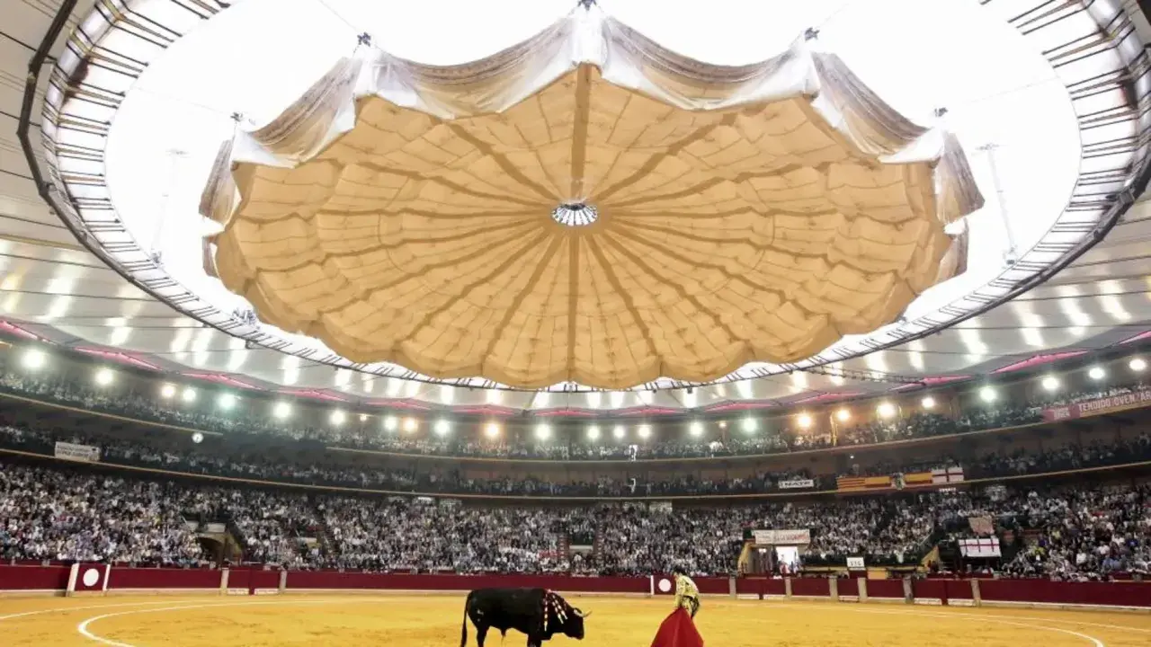 Un torero y un toro en la arena de la plaza de toros La Misericordia, con el público en las gradas y un llamativo techo desplegable.