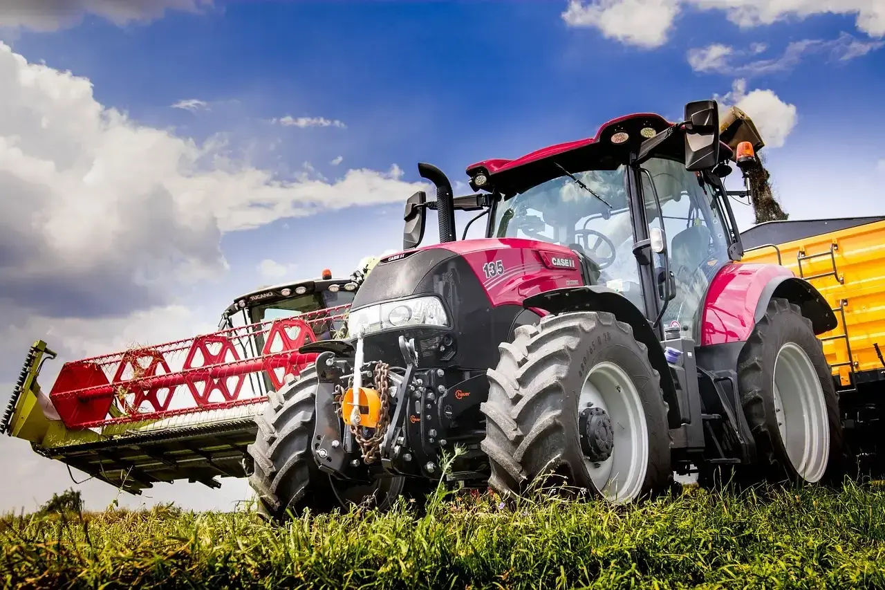 Czerwony traktor Case IH z hederem żniwnym i żółtą przyczepą. Warto wiedzieć, jak wymienić olej w takim sprzęcie, by służył latami.