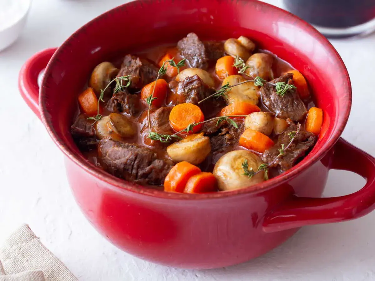 Un plat rouge rempli de bœuf bourguignon facile, avec des morceaux de bœuf tendres, des carottes et des champignons, garni de thym frais.