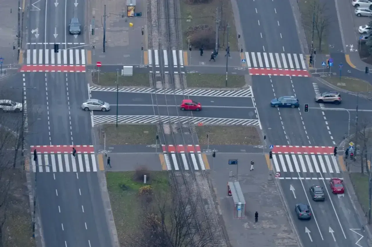 Skrzyżowanie z przejściami dla pieszych. Czerwony samochód wykonuje wyprzedzanie na pasach, ignorując pieszych.