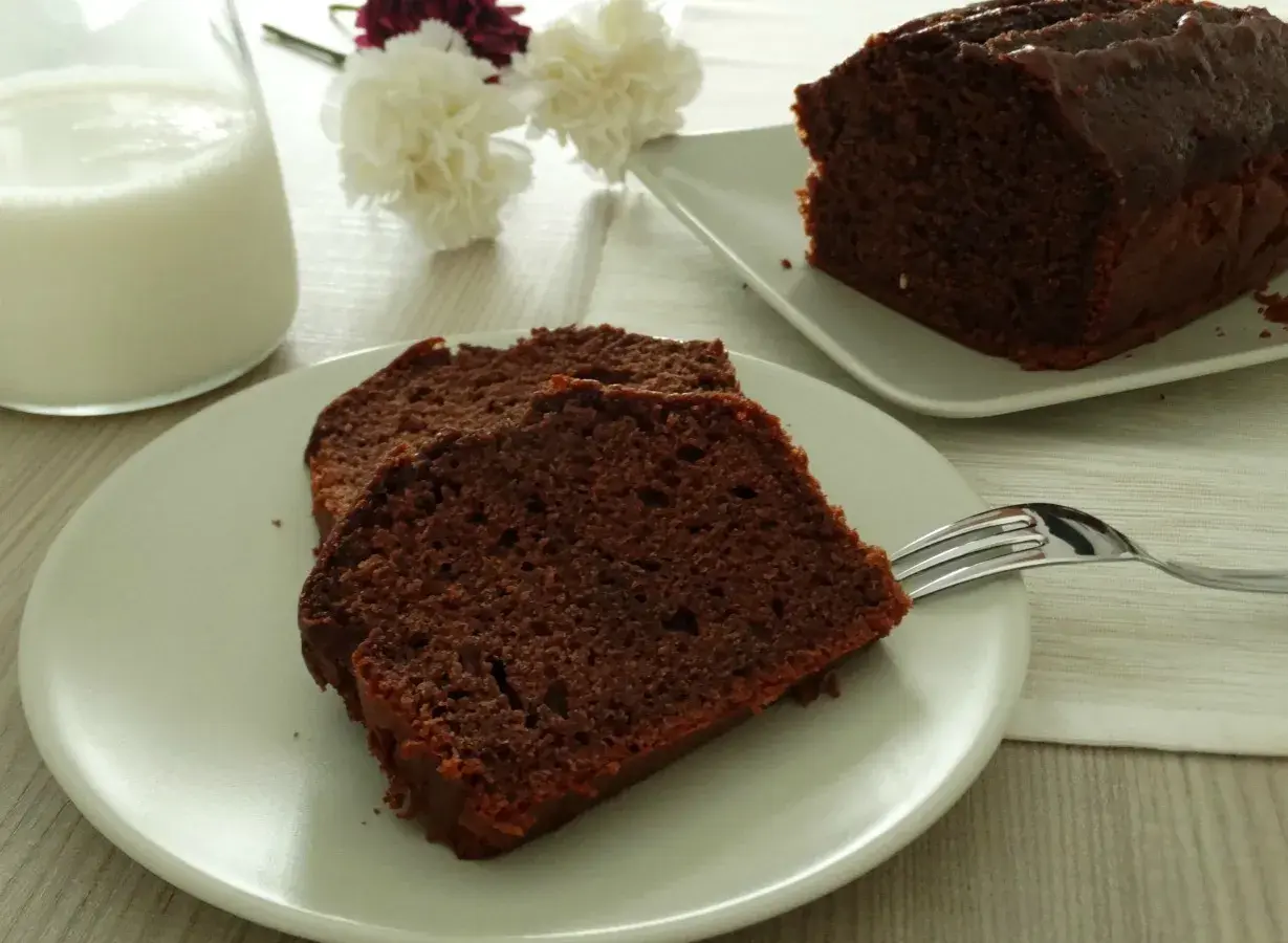 Fette di plumcake al cioccolato su un piatto, con una forchetta e un bicchiere di latte sullo sfondo.
