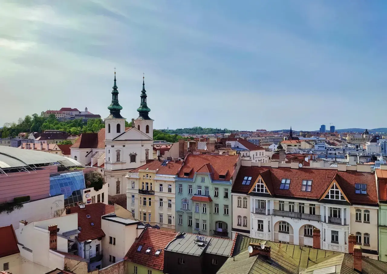 Widok na dachy Brna, w tym kościół z zielonymi wieżami i zamek na wzgórzu. Idealne miejsce, by zobaczyć, co w Brnie warto zobaczyć.