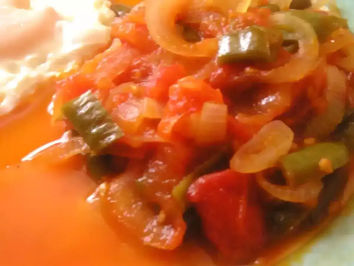 Une assiette de piperade recette, avec des poivrons verts, des oignons et des tomates mijotés, à côté d'un œuf au plat.