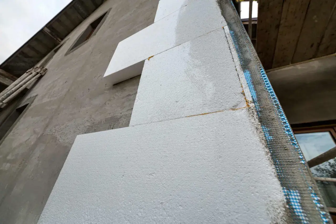 Pannelli di polistirolo applicati su una parete grezza, un passo fondamentale per come isolare una parete esterna. Rete e malta in vista.