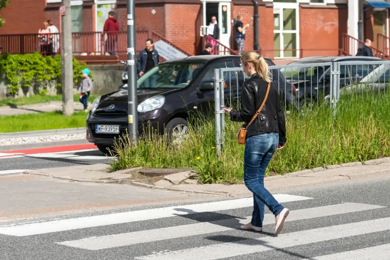 Młoda kobieta, pieszy, idzie przez pasy, patrząc w telefon.