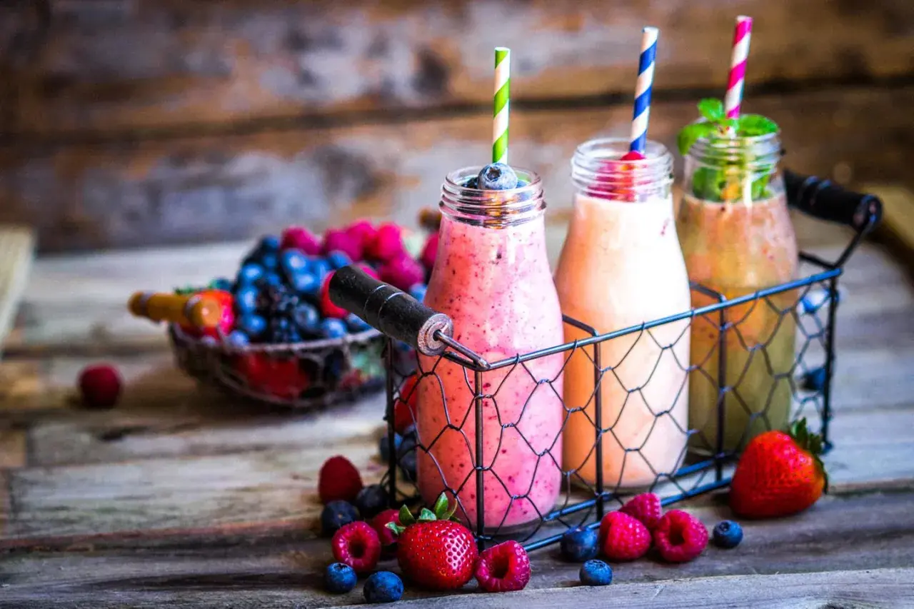 Drei bunte Flaschen mit leckeren Smoothies zum Abnehmen, umgeben von frischen Beeren und Erdbeeren auf rustikalem Holz.