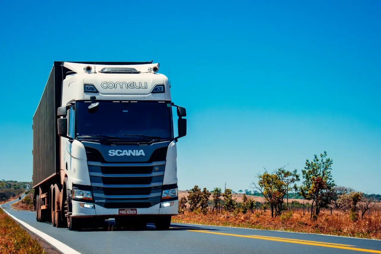 Biała ciężarówka Scania z naczepą jedzie po pustej drodze. Kierowca c. zarabia na życie, przewożąc towary.
