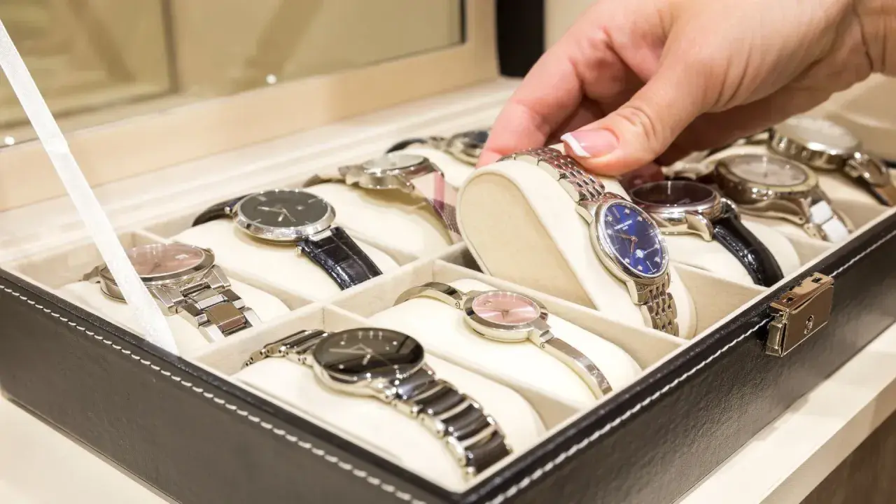 Una mano elige un reloj de una caja. Los relojes de pulsera, algunos de niquel que no se oxida, están ordenados en compartimentos.