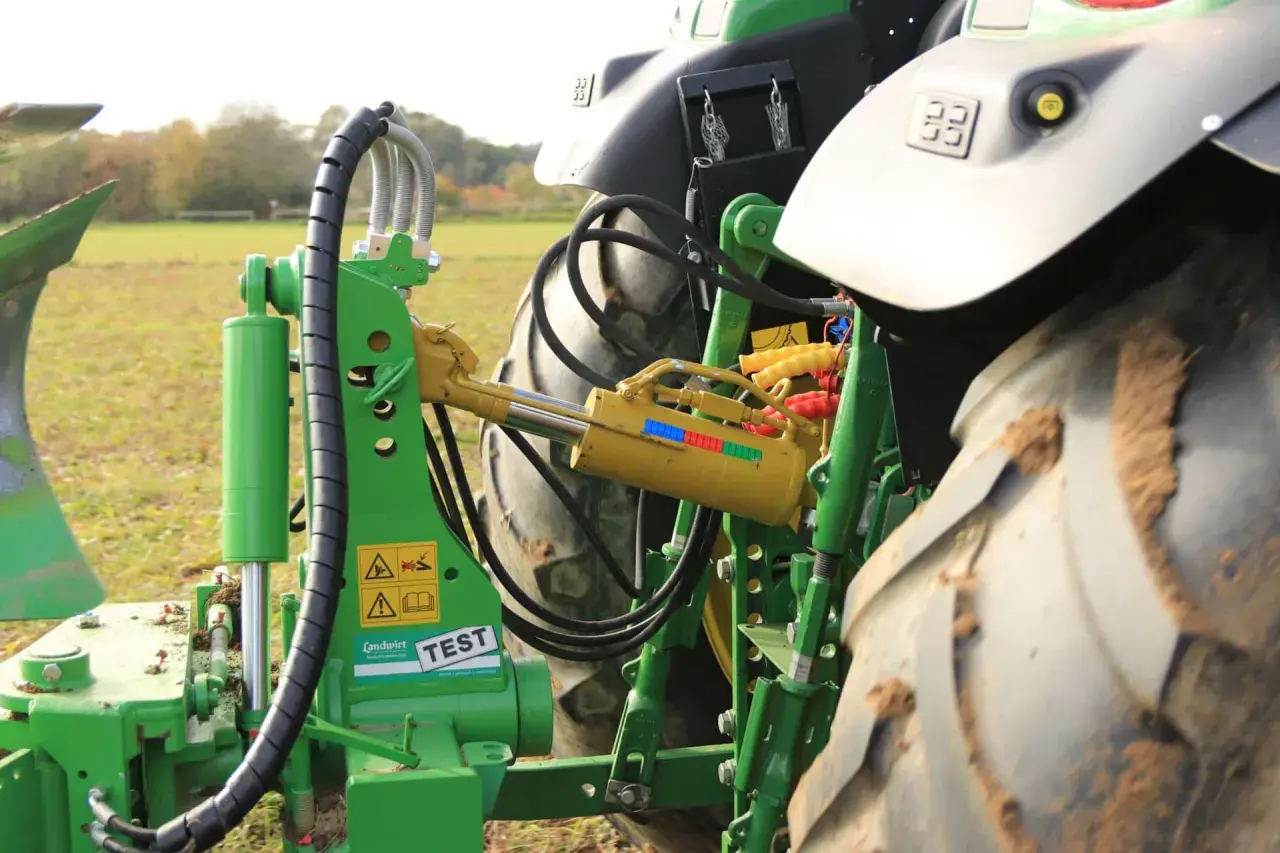 Grüner Traktor mit angehängtem Pflug. Ein gelber Walterscheid Oberlenker mit Hydraulikzylinder ist sichtbar.