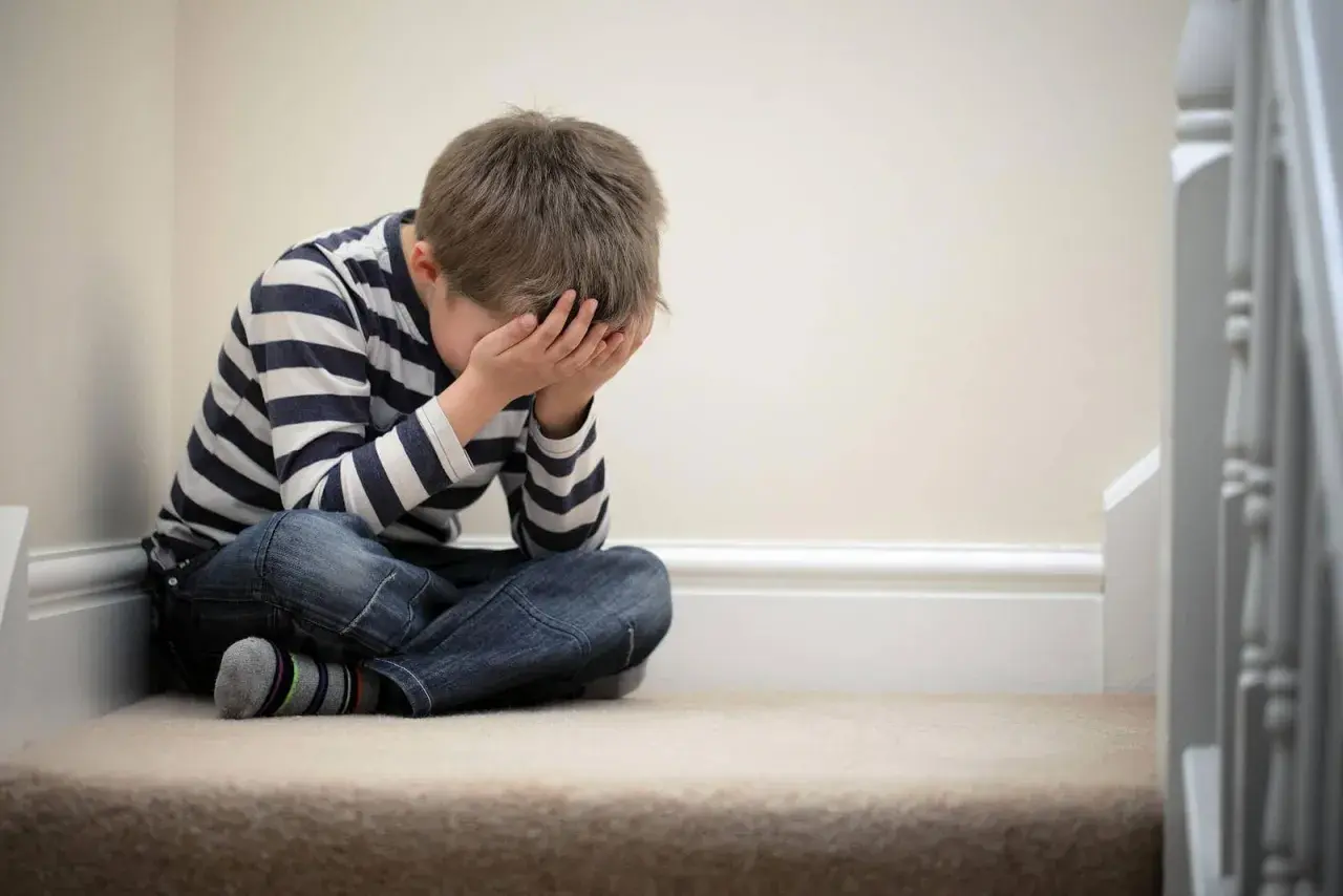 Bambino seduto sulle scale, con le mani sul viso, simbolo della delusione dei figli.