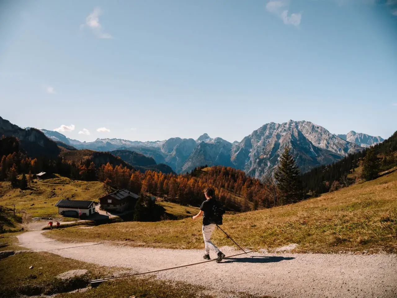 A lone hiker enjoys a scenic autumn day hiking in Bavaria, with colorful trees and majestic mountains in the background.