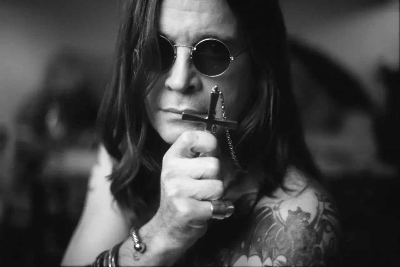 Ozzy Osbourne, ikona zespołu Black Sabbath, w okularach i z krzyżem w dłoni.