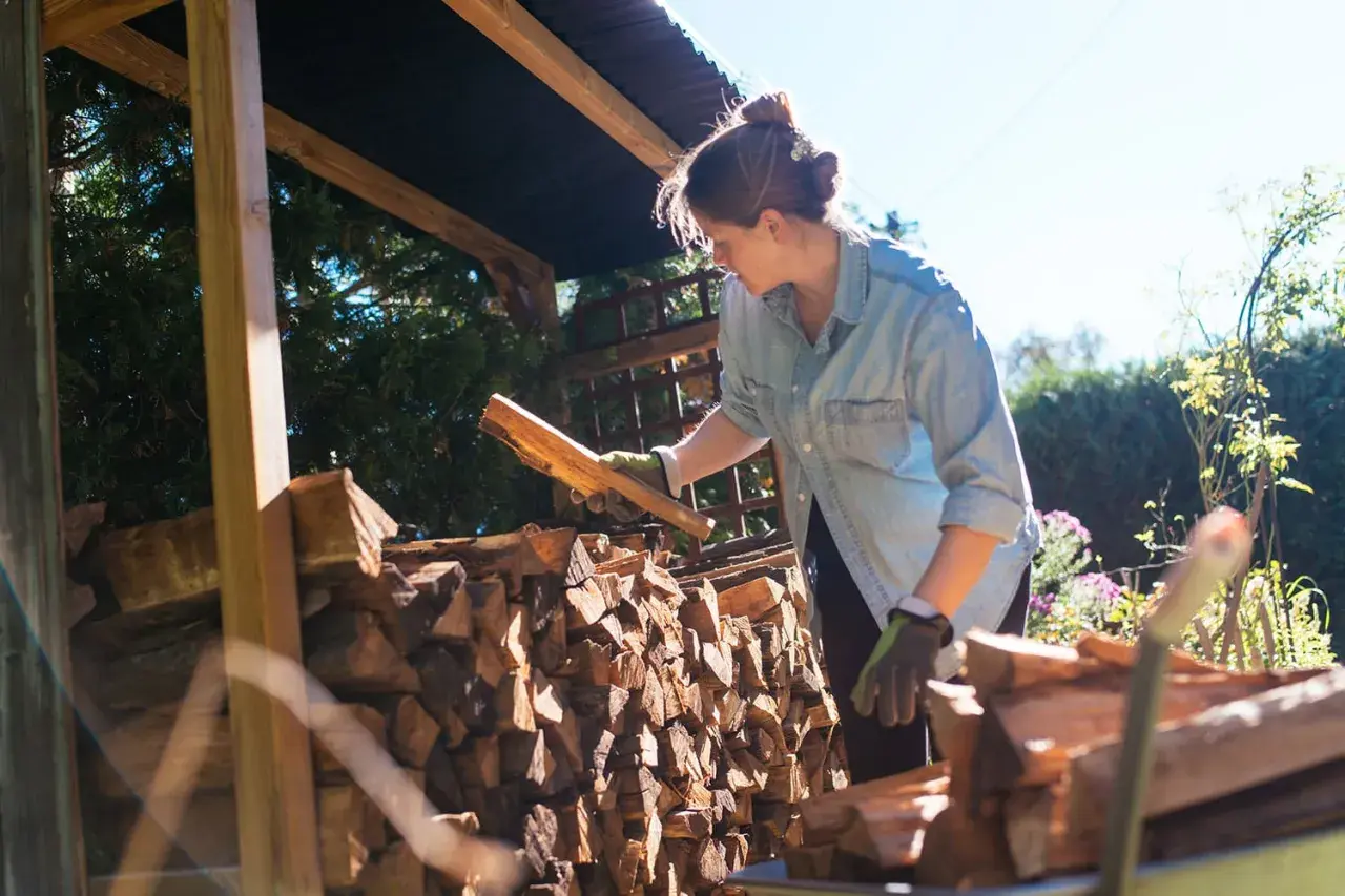 Femme avec des bûches de bois sous un abri.