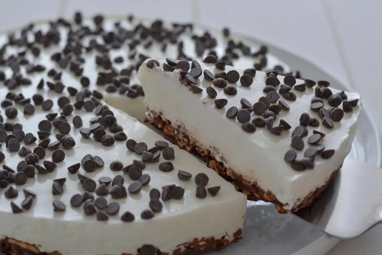 Una fetta di torta fredda allo yogurt, ricoperta di gocce di cioccolato, viene servita da una spatola.