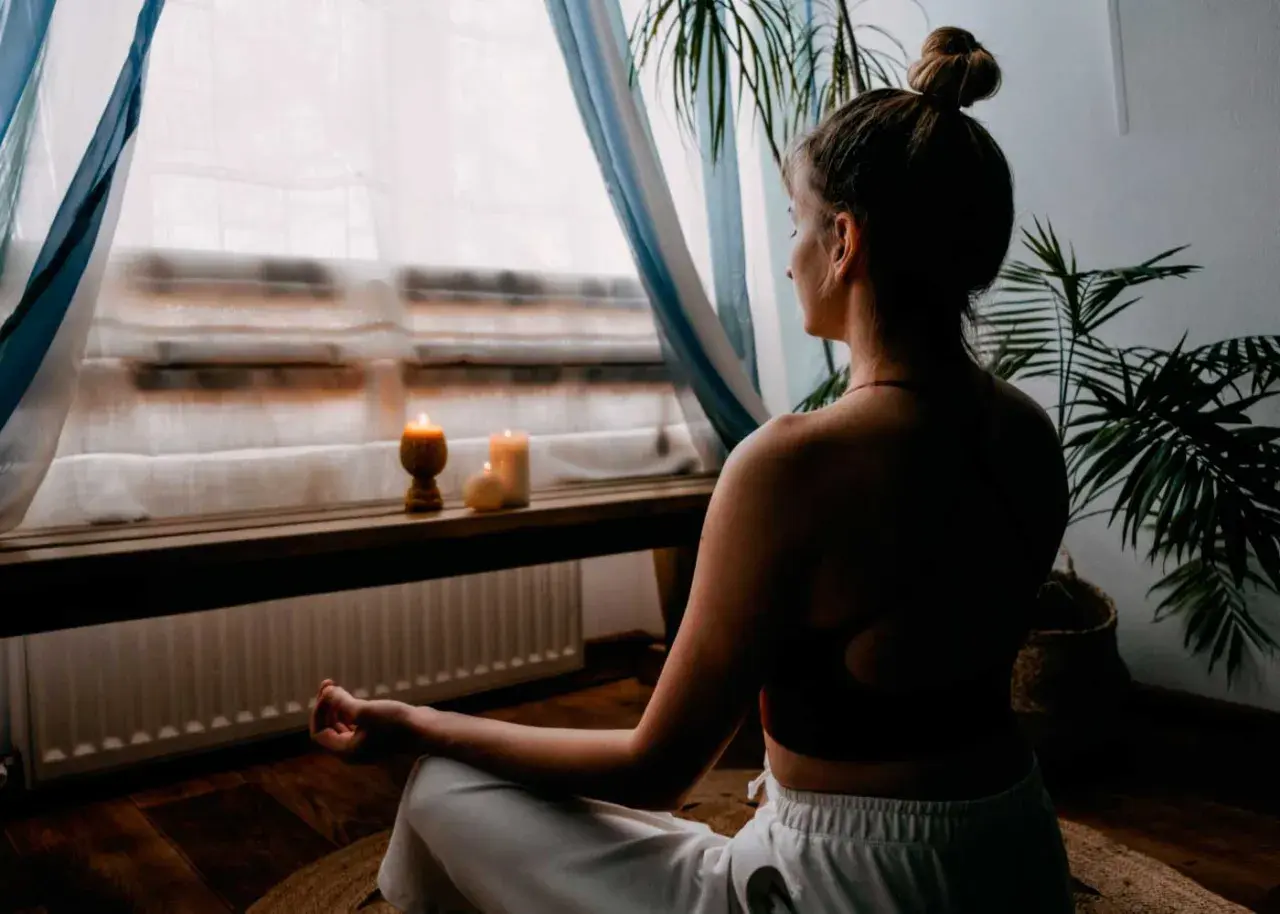 Mujer meditando en un espacio para meditar en casa, con velas encendidas y plantas.