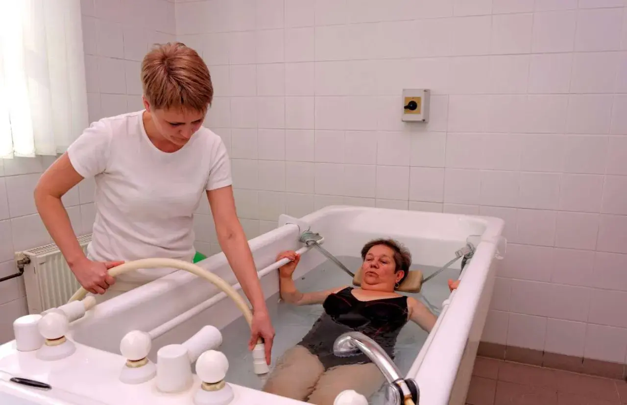 Therapeutin führt Balneotherapie bei Arthrose durch. Eine Frau liegt in einem Wasserbad, während die Therapeutin eine Düse hält.