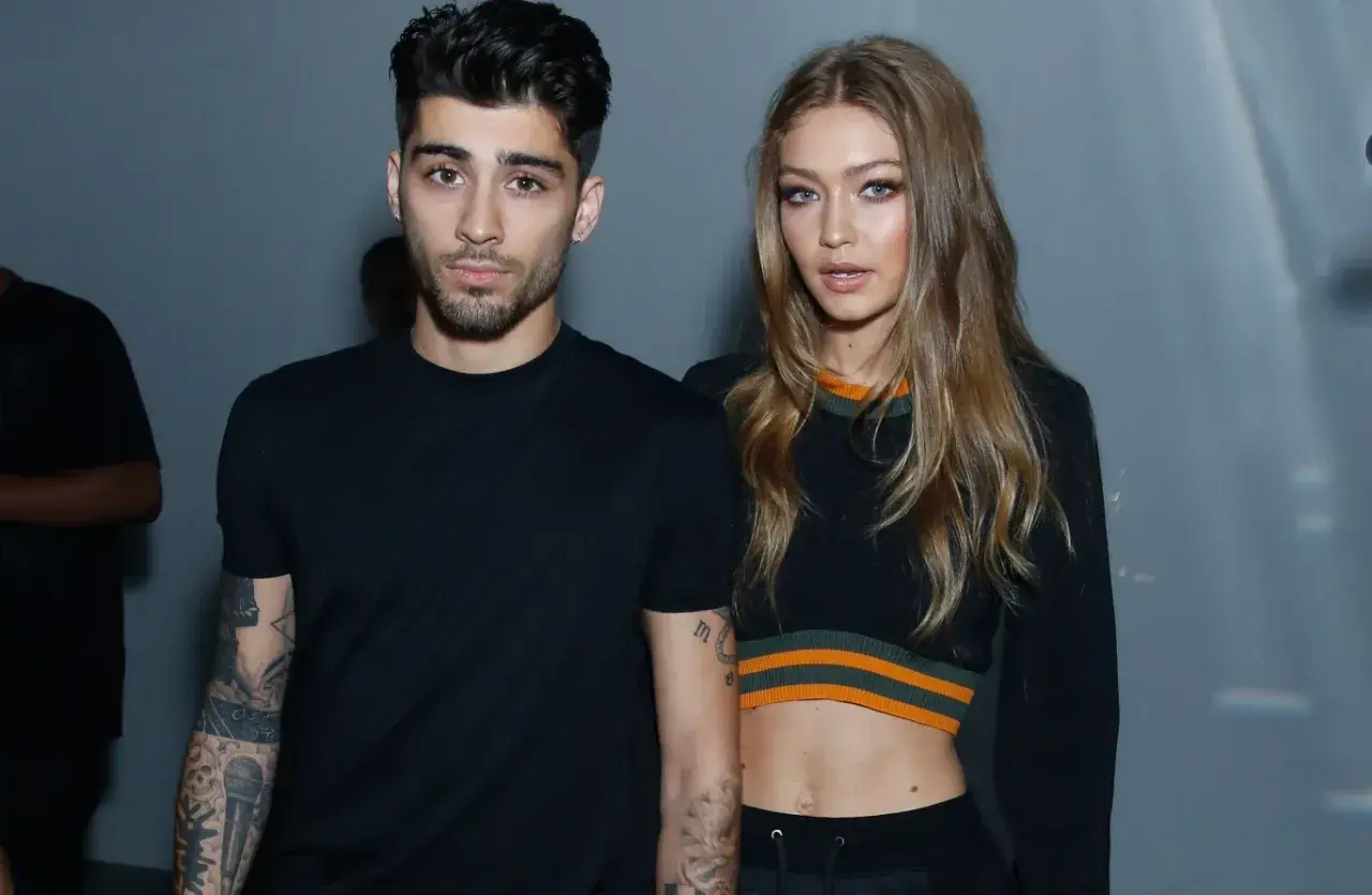 Zayn Malik i Gigi Hadid pozują razem, oboje ubrani na czarno. Zayn ma tatuaże na ramionach, a Gigi odsłania brzuch w krótkim topie.